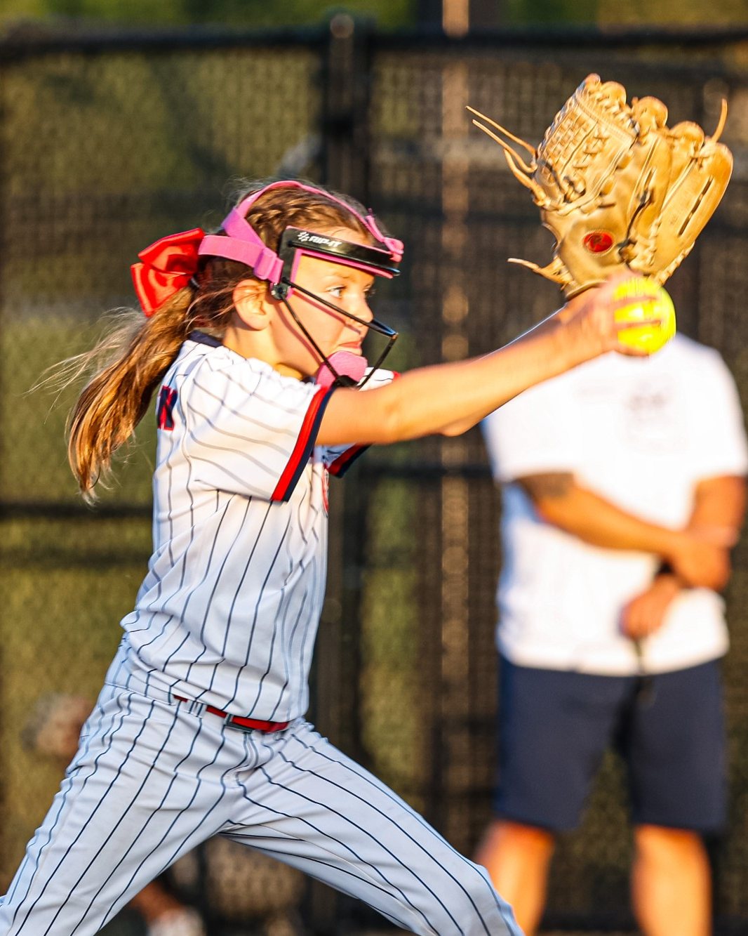 Genevieve pitching in a pinstripe uniform at golden hour